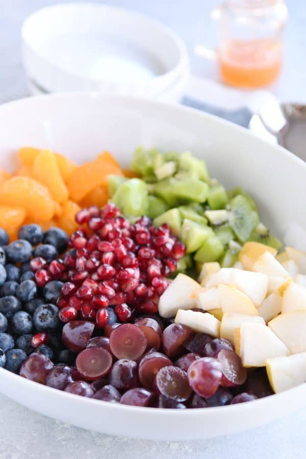 El tazón blanco contiene uvas, arándanos, peras, kiwis, naranjas y semillas de granada, lo que es conveniente para ensaladas de frutas frescas en invierno.