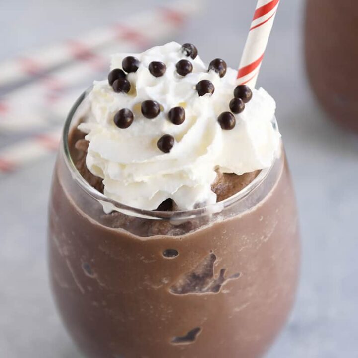 Chocolate caliente congelado en vaso transparente con nata montada y pajitas.