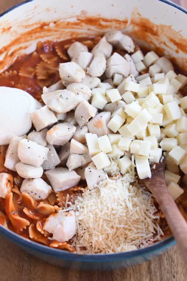 Bloque de queso mozzarella, pollo cocido, queso parmesano y queso ricotta, y pasta de pajarita en una sartén de hierro fundido