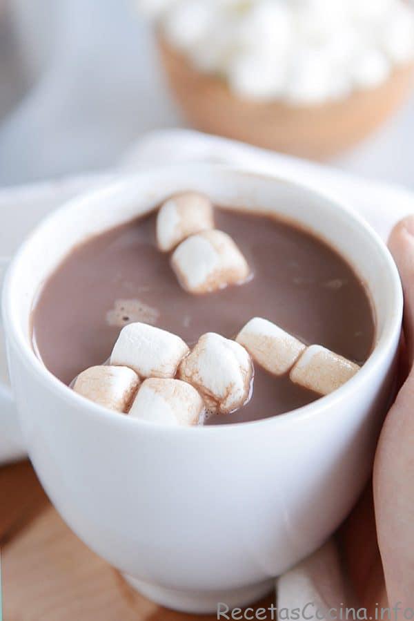 Una taza blanca con chocolate caliente humeante y malvaviscos flotando sobre ella.