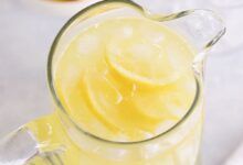 Vista superior de un frasco de vidrio de limonada casera y un tazón de jugo de limón.