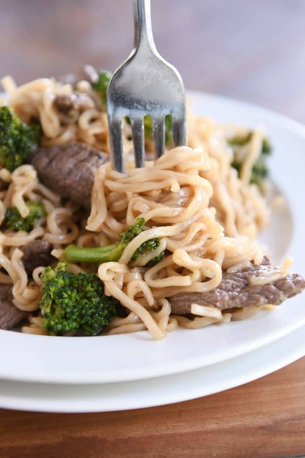 Gire los fideos ramen en un tenedor con carne y brócoli en un plato blanco.