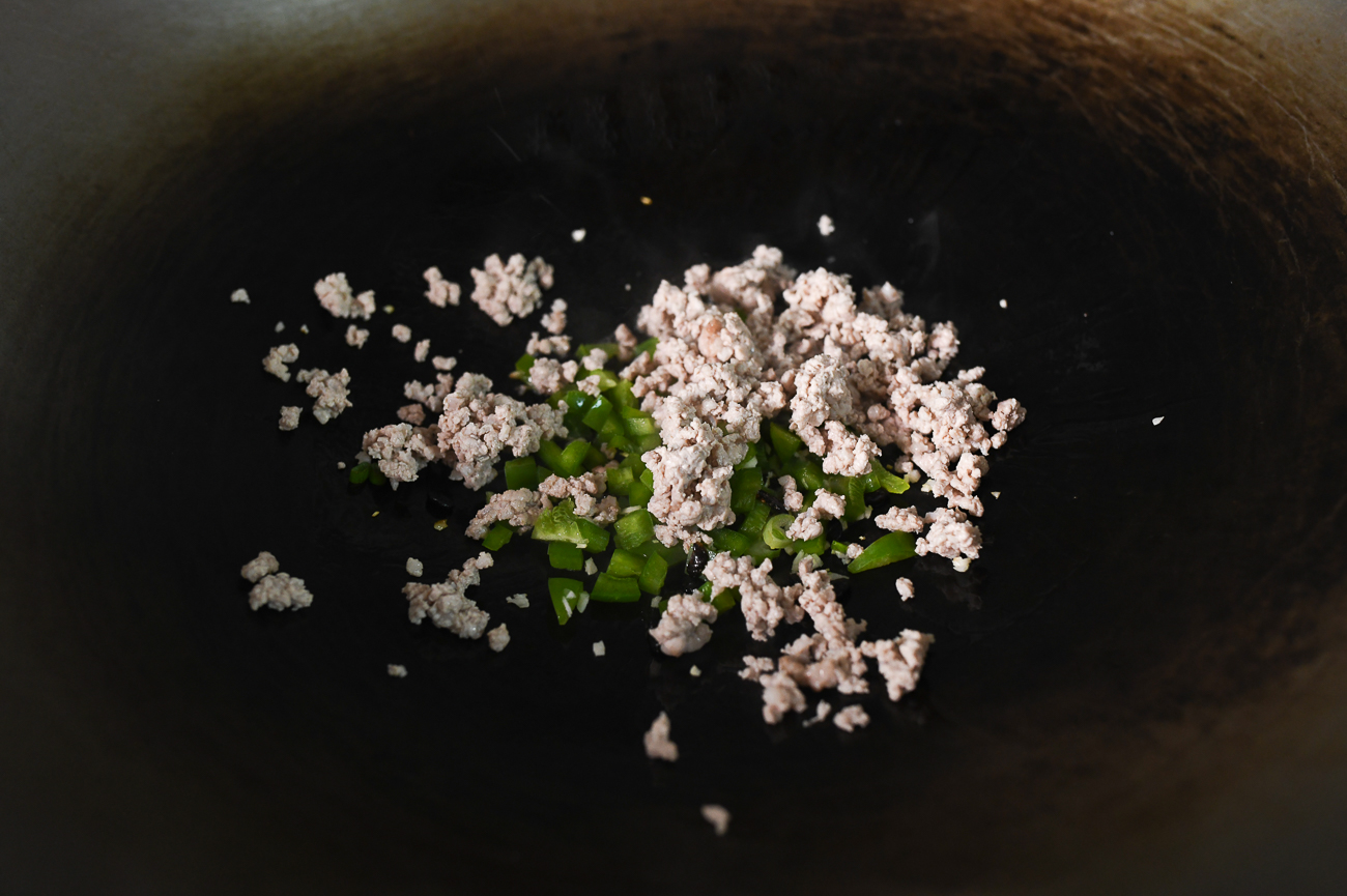 Pimientos morrones, carne de cerdo molida y otros ingredientes en el wok