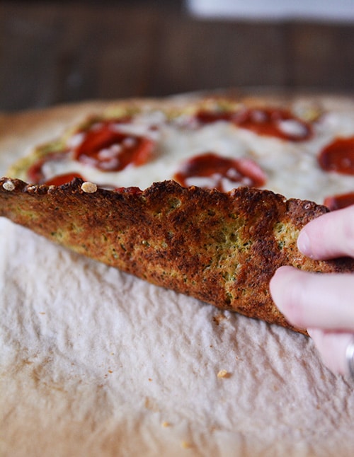 Levante la pizza con una mano, mostrando la parte inferior de la piel del calabacín cocido.