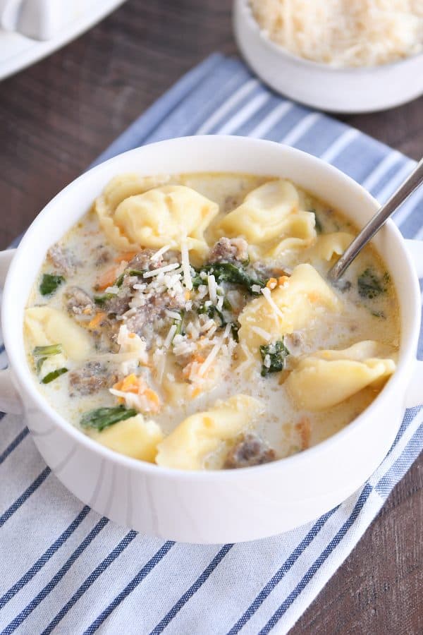 Sopa de espinacas con tortellini y salchicha en un bol blanco con cuchara y olla de cocción lenta.