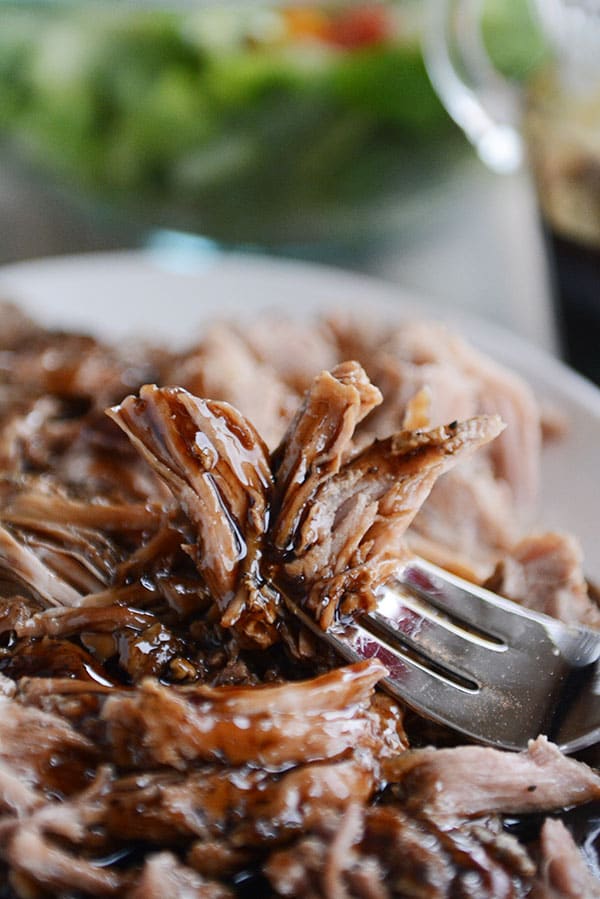 Se coloca un tenedor de cerdo desmenuzado sobre un plato entero de cerdo con una ensalada de fondo. 