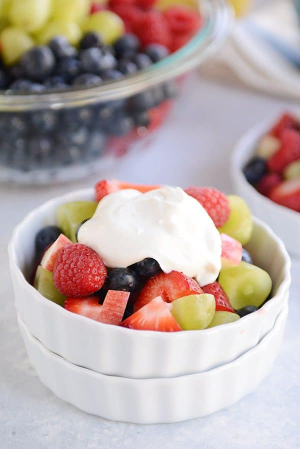 Un tazón blanco relleno con ensalada de frutas frescas, cubierto con yogur de vainilla