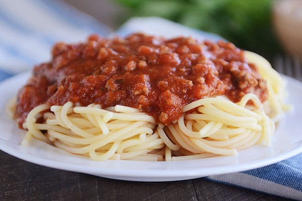 Salsa de espagueti casera sobre espaguetis cocidos, llenando un plato blanco grande
