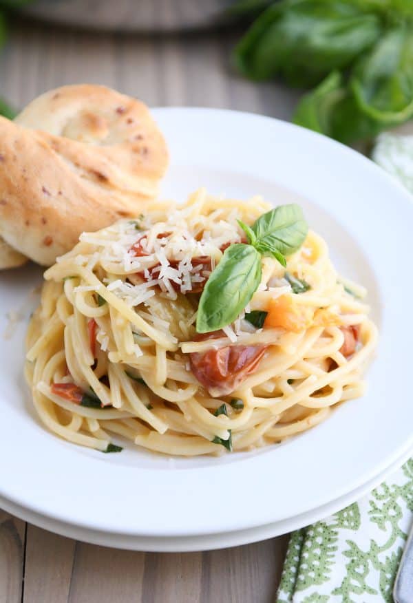 Una olla de espaguetis cremosos de tomate y albahaca en un plato blanco, cubierto con palitos de pan de Parma.