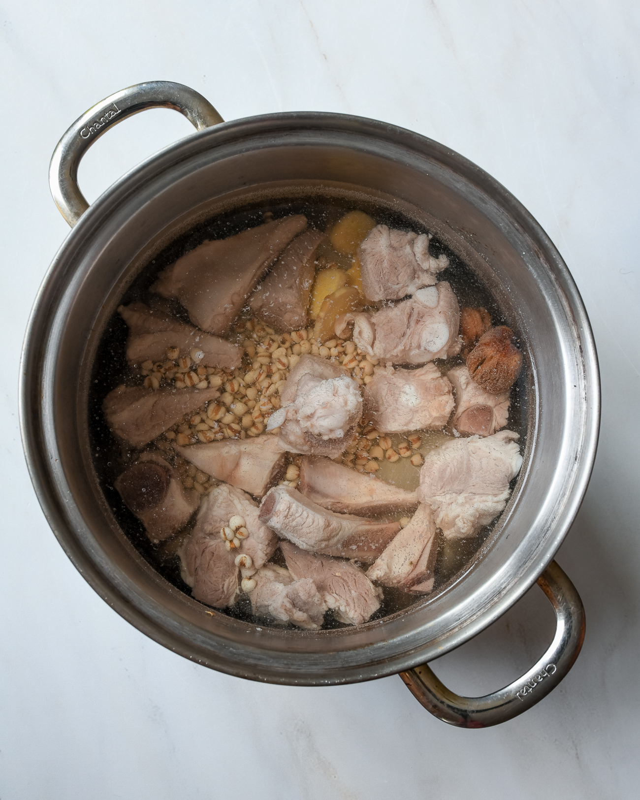 Huesos de cerdo escaldados con cebada, jengibre y dátiles en una olla sopera