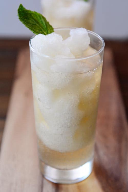 Un vaso alto lleno de limonada de menta, con una hoja de menta insertada al lado. 