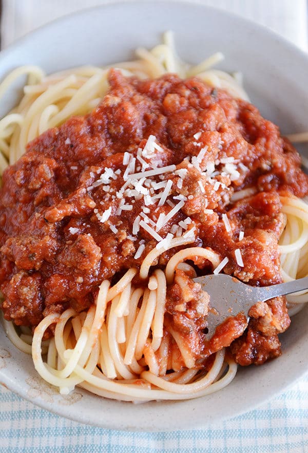 Use un tenedor para hacer girar un bocado de espagueti en un tazón blanco con salsa de espagueti con carne y queso parmesano en los fideos.