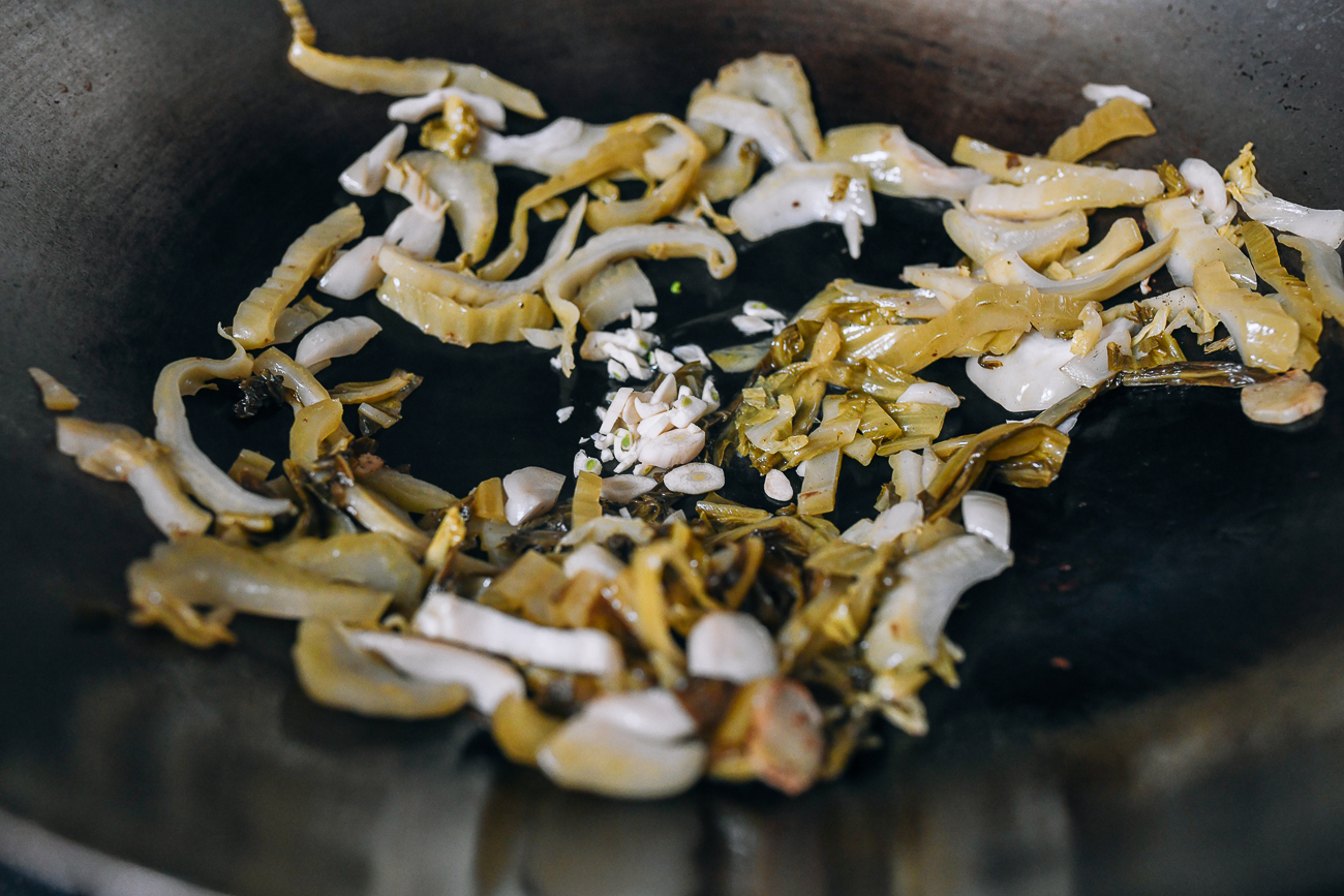 Agregue ajo a las hojas de mostaza en escabeche en el wok.