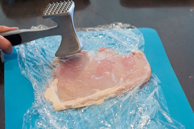 Use un ablandador de carne para machacar la pechuga de pollo en la envoltura de plástico en una forma plana.