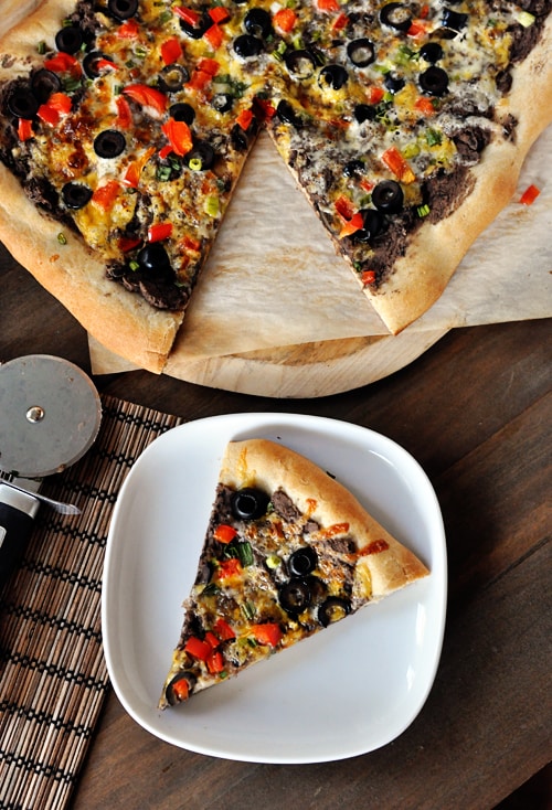 Vista superior de la pizza de frijoles negros con verduras en la parte superior, tome una rebanada en un plato blanco