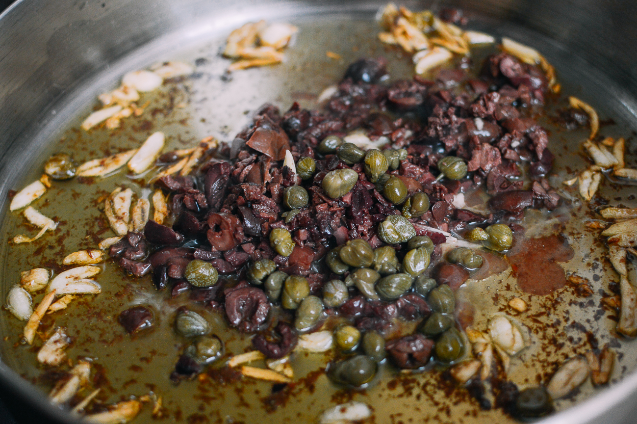 Aceitunas, alcaparras, anchoas y ajos en aceite de oliva en una sartén