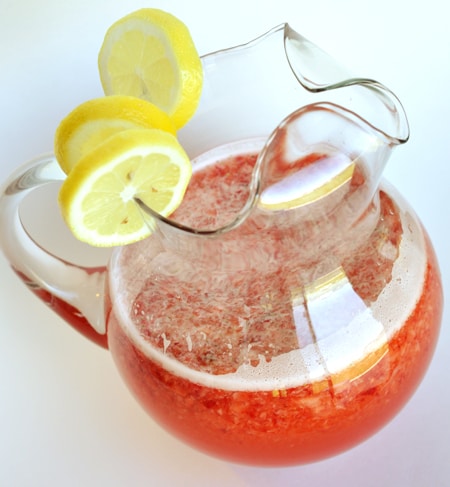Frasco de vidrio con rodajas de limón y limonada de fresa medio llena encima