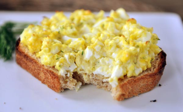 Sándwich de ensalada de huevo de cara abierta con un bocado en un plato blanco