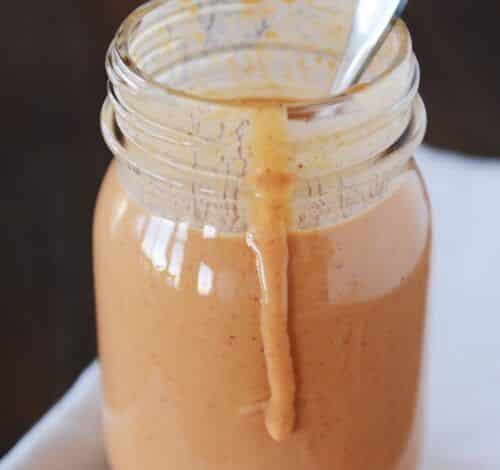 Un tarro de cristal lleno de salsa marrón claro, con una cuchara, chorreando agua por un lado.