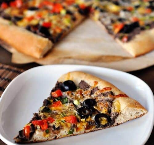 Se coloca un trozo de pizza de frijoles negros y verduras en un plato blanco, y el resto de la pizza se coloca detrás del plato.