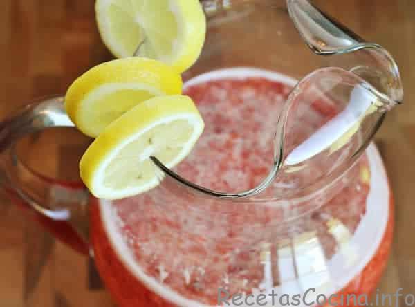 Vista superior de una jarra de vidrio llena de limonada de fresa con rodajas de limón a un lado