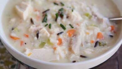 Un plato blanco de sopa de pollo y arroz salvaje con una cuchara al lado.