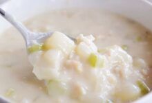 Use una cuchara para tomar un bocado grande de sopa de almejas del tazón blanco.
