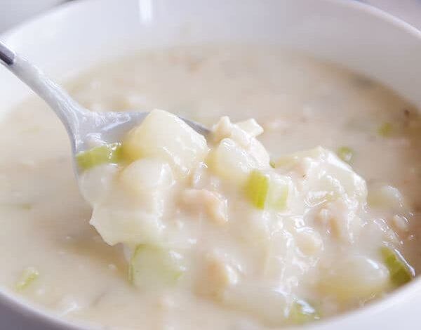 Use una cuchara para tomar un bocado grande de sopa de almejas del tazón blanco.