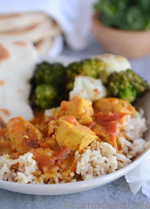 Un plato blanco de arroz cubierto con pollo al curry y verduras. 