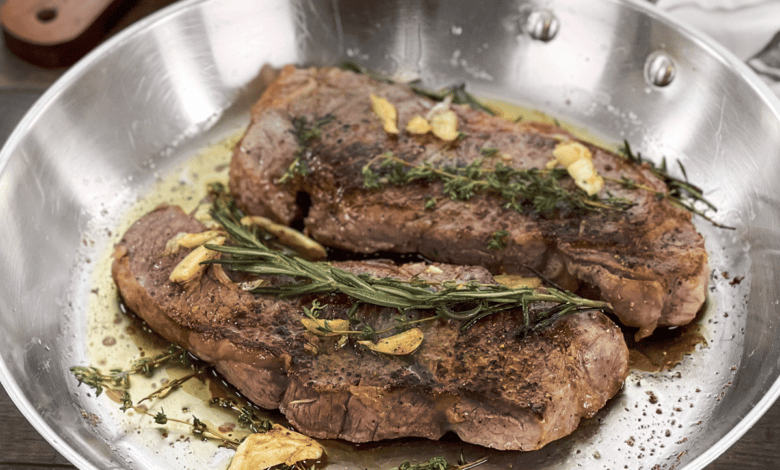 New York strip steaks in a pan with butter, garlic, and rosemary.