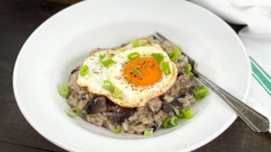 Mushroom breakfast risotto in a white dish, topped with a fried eggs and green onion.