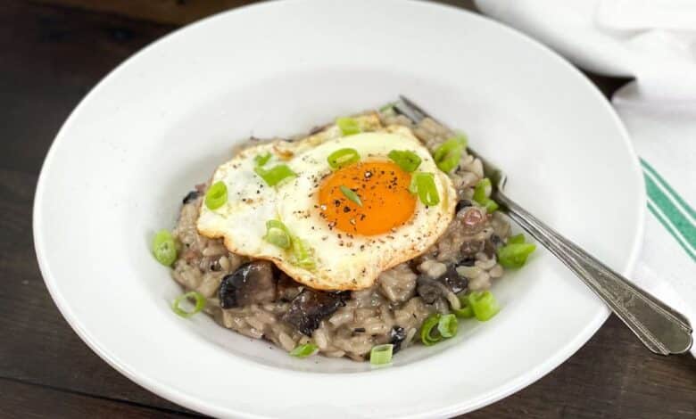Mushroom breakfast risotto in a white dish, topped with a fried eggs and green onion.