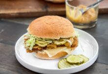 White plate with crispy chicken sandwich with cheese, lettuce, pickles and extra pickles on the plate.