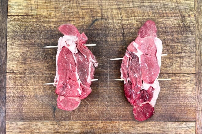 Dos bistecs de chuck eye crudos que se mantienen juntos con brochetas de madera.