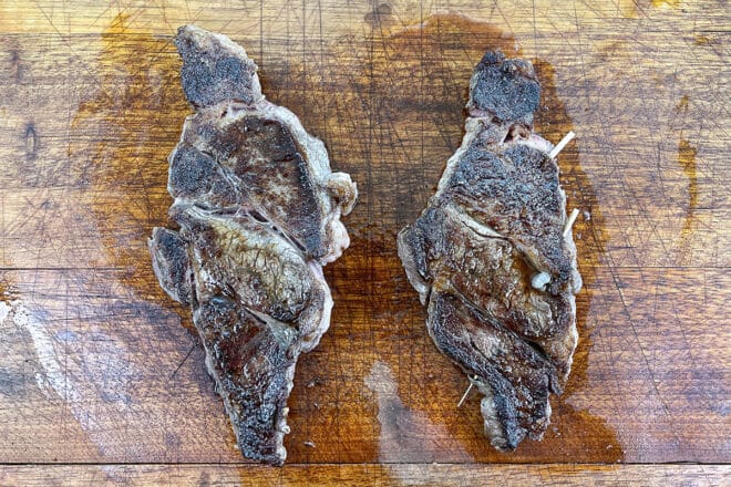 Filetes de chuck eye cocidos en una tabla de cortar, uno con brochetas y otro sin ellas.