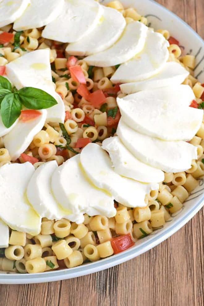 Ensalada de pasta Caprese Ensalada de pasta Caprese en un tazón para servir, cubierta con rebanadas de mozzarella fresca y hojas de albahaca.