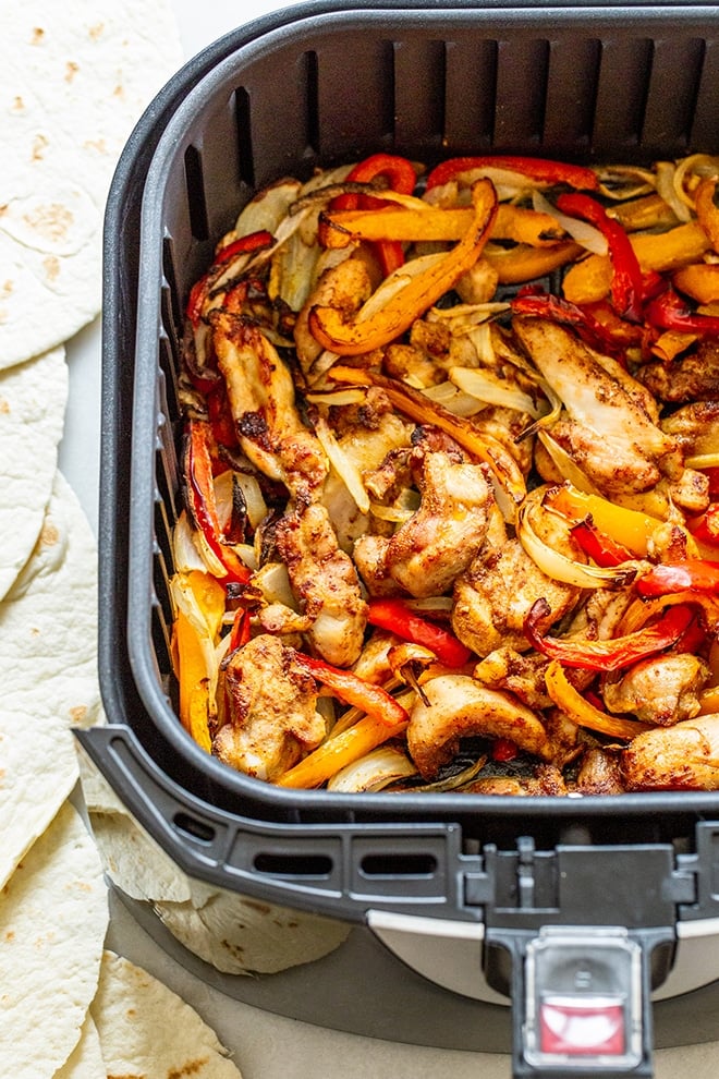 Fajitas de pollo con freidora Pollo en rodajas, pimientos rojos y amarillos y cebollas con condimento para fajitas en la cesta de una freidora.